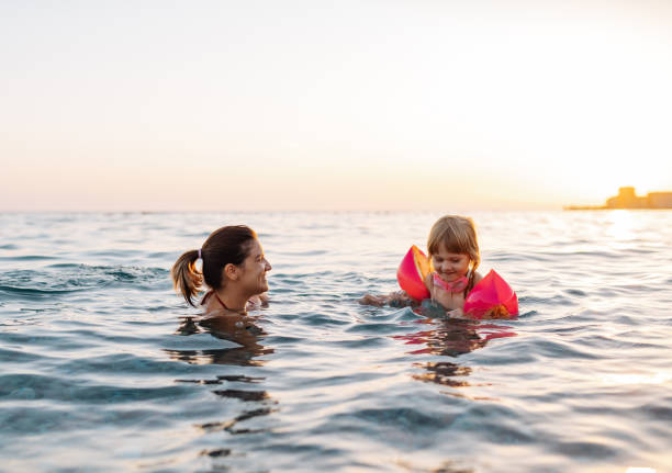 bambina di tre anni che nuota in mare imparando a nuotare, indossando ali d'acqua - women courage water floating on water foto e immagini stock