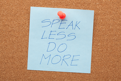 Speak less do more phrase on note pinned on cork board.