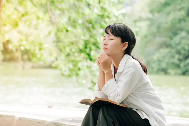 Photo of Woman praying in the morning on nature background.Hands folded in prayer on a Holy Bible in church concept for faith, spirituality and religion