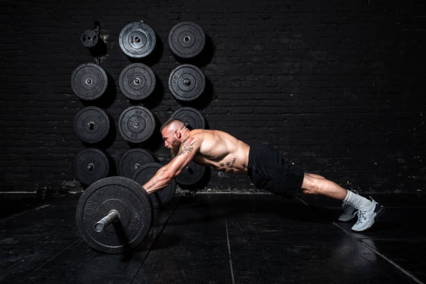 istock Young strong fit sweaty muscular man with big muscles doing abs workout by rolling barbell weights in the floor of the gym as hardcore cross training 1272245634