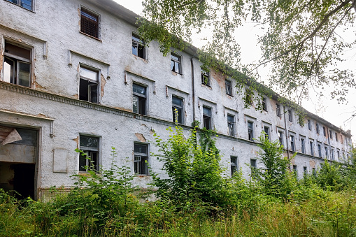 Exterior of an old abandoned hospital building overgrown with grass and greenery