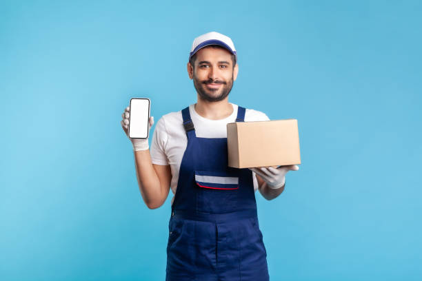 istock Cargo tracking mobile app. Courier man in uniform holding cardboard box and cellphone 1272251938