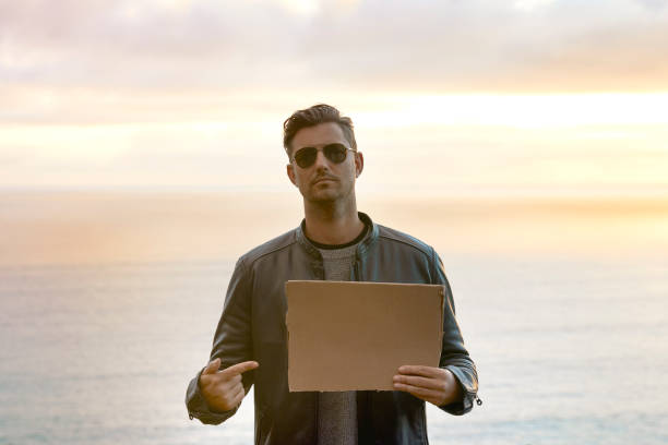 istock Handsome man pointing at blank cardboard with scenic background 1272253045