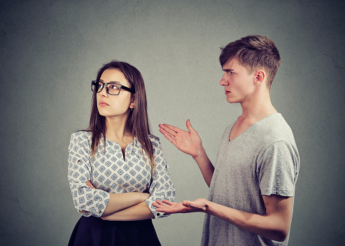 Young woman looking offended while arguing with man in misunderstand on gray background