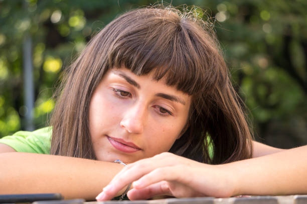 A young woman si sitting outside and has her head resting on the table.  She looks like daydreaming or absorbed in thoughts.