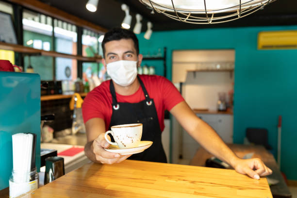 istock Young man  working at cafe shop with a face mask and giving caffee cup 1272258194