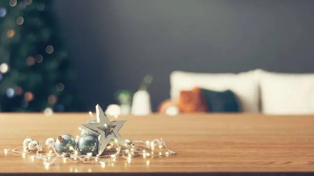 Christmas ornaments on wooden table top in living room with christmas tree blur background.
