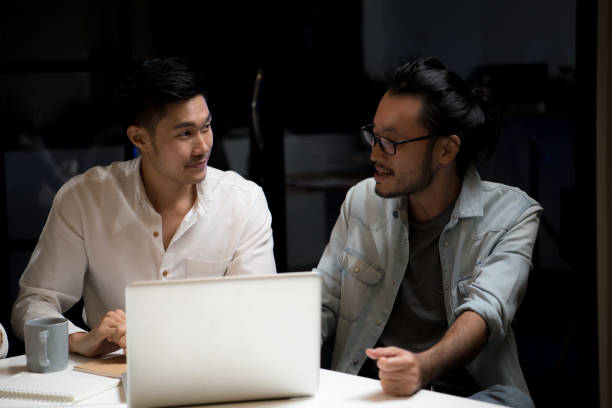 istock Two Asian businessmen using a computer to discuss work in the office at night 1272261418