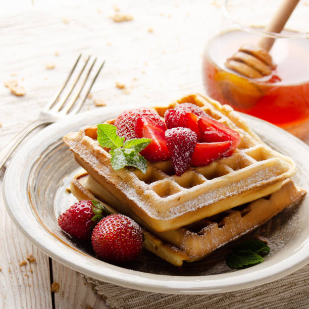 istock Belgian waffles served with strawberries and mint leaf dusted with powdered sugar on white wooden kitchen table with syrup aside 1272262984