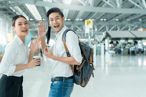 two attractive asian businessman and businesswoman hand gesture wave greeting and goodbye social distancing in departure airport terminal