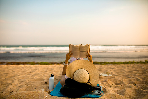 Asian young woman relaxing and lying on the sand enjoying the sunset