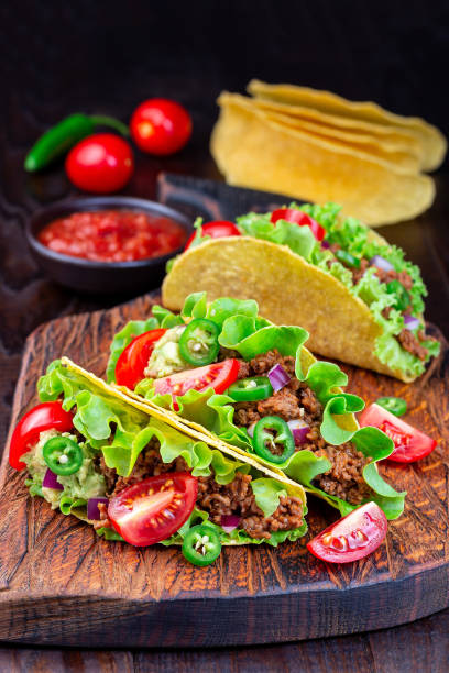 istock Taco shells with ground beef meat,  mashed avocado, tomato, lettuce, red onion and jalapeno pepper, vertical, on wooden board 1272267913
