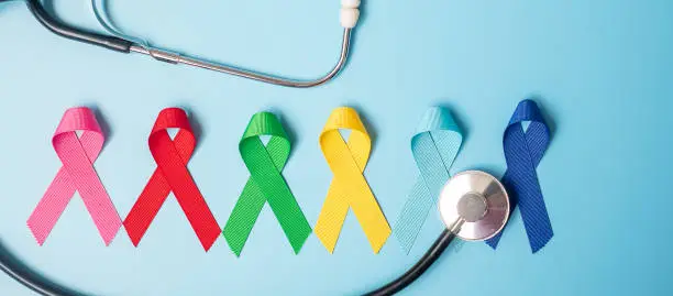 Photo of World cancer day (February 4). colorful awareness ribbons; blue, red, green, pink and yellow color on wooden background for supporting people living and illness. Healthcare and medicine concept