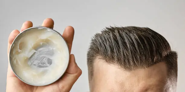 Man applying a clay, pomade, wax, gel or mousse from round metal box for styling his hair after barbershop hair cut. Advertising concept of mans products. Treatment and care against lost of hair.