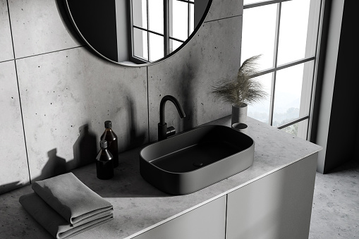 Top view of modern sink with round mirror standing in stylish bathroom with gray and tiled walls and concrete floor. 3d rendering