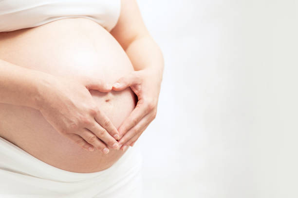 Pregnant woman hold heart-shaped hands on her baby bumps skin. Copyspace for your text. stock photo