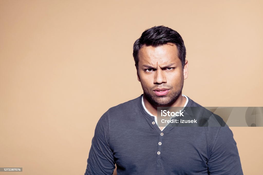 Suspicious businessman over brown background Portrait of suspicious entrepreneur with raised eyebrow. Male business person standing against brown background. He is wearing t-shirt. Colored Background Stock Photo