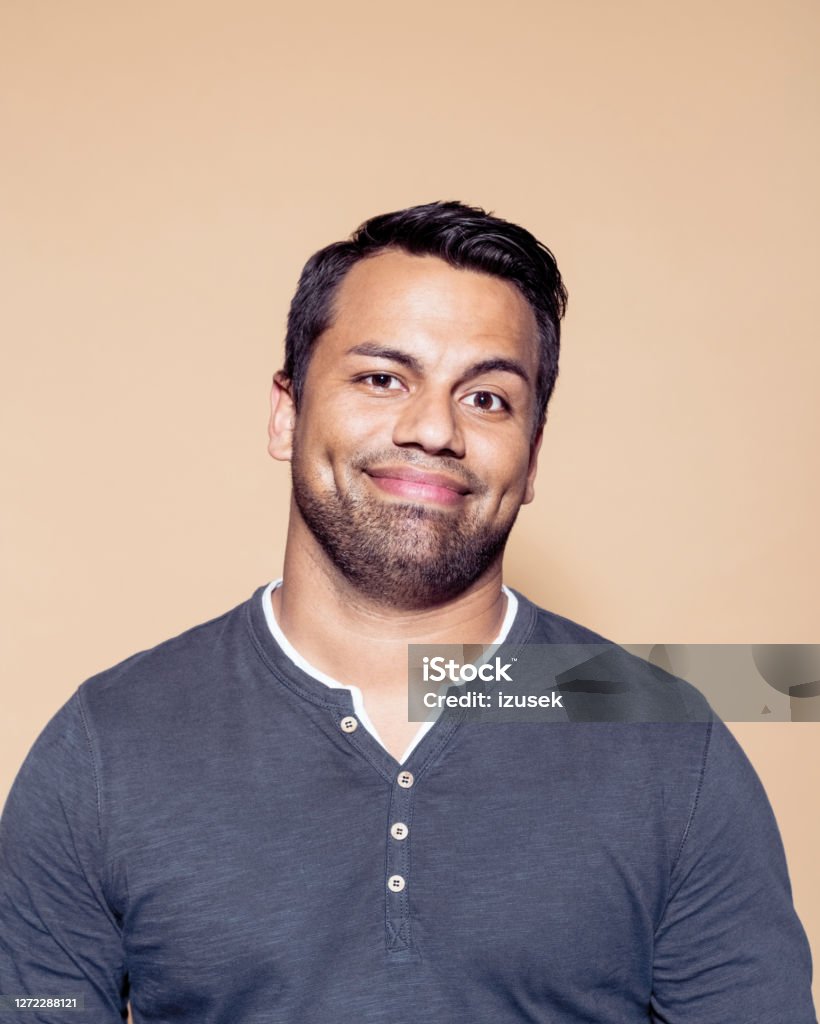 Confident smiling businessman on brown background Portrait of smiling entrepreneur with raised eyebrow. Confident businessman standing against colored background. He is wearing gray t-shirt. 25-29 Years Stock Photo