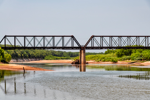 A railway trestle  crossing the Red River between the U.S. states of Texas and Oklahoma on a bright summer afternoon.