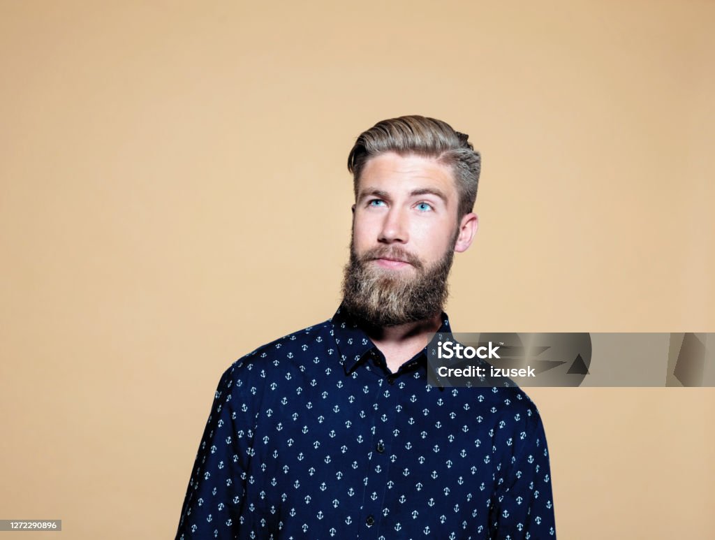 Thoughtful businessman over brown background Thoughtful businessman looking away. Male entrepreneur standing against brown background. He is wearing blue shirt. Brown Background Stock Photo