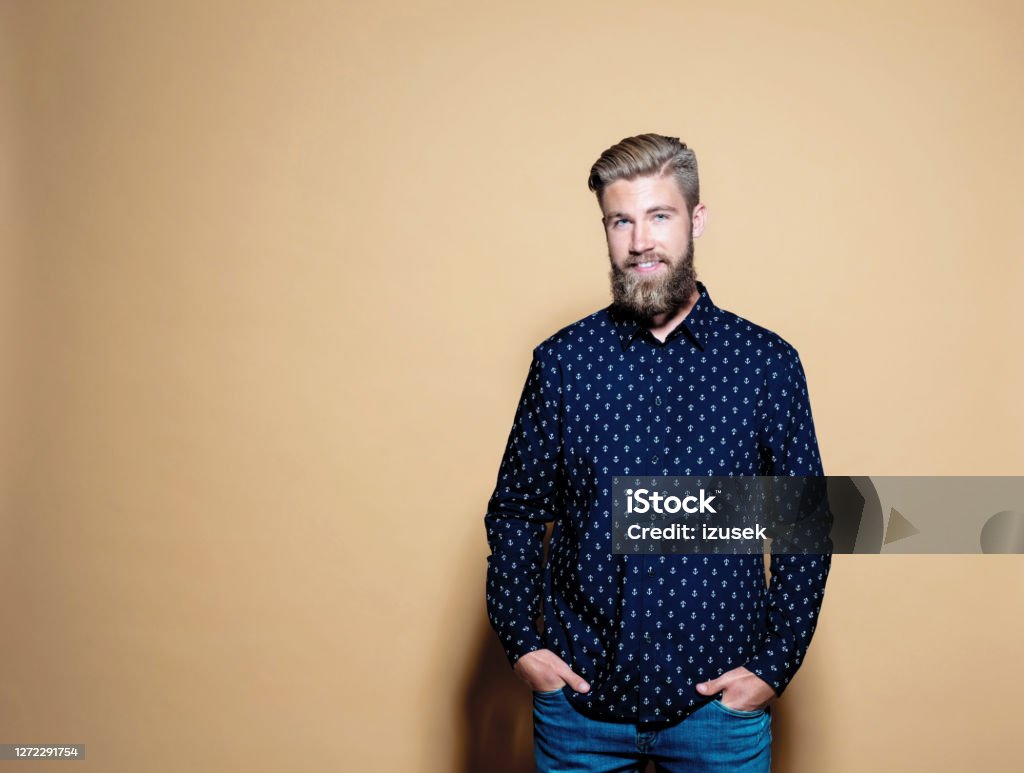 Smiling businessman over brown background Portrait of smiling entrepreneur with hands in pockets. Businessman standing against brown background. He is in shirt and jeans. Portrait Stock Photo