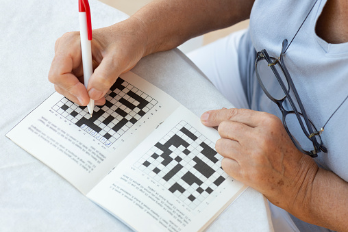 Close up of a senior woman hands doing crossword puzzle.