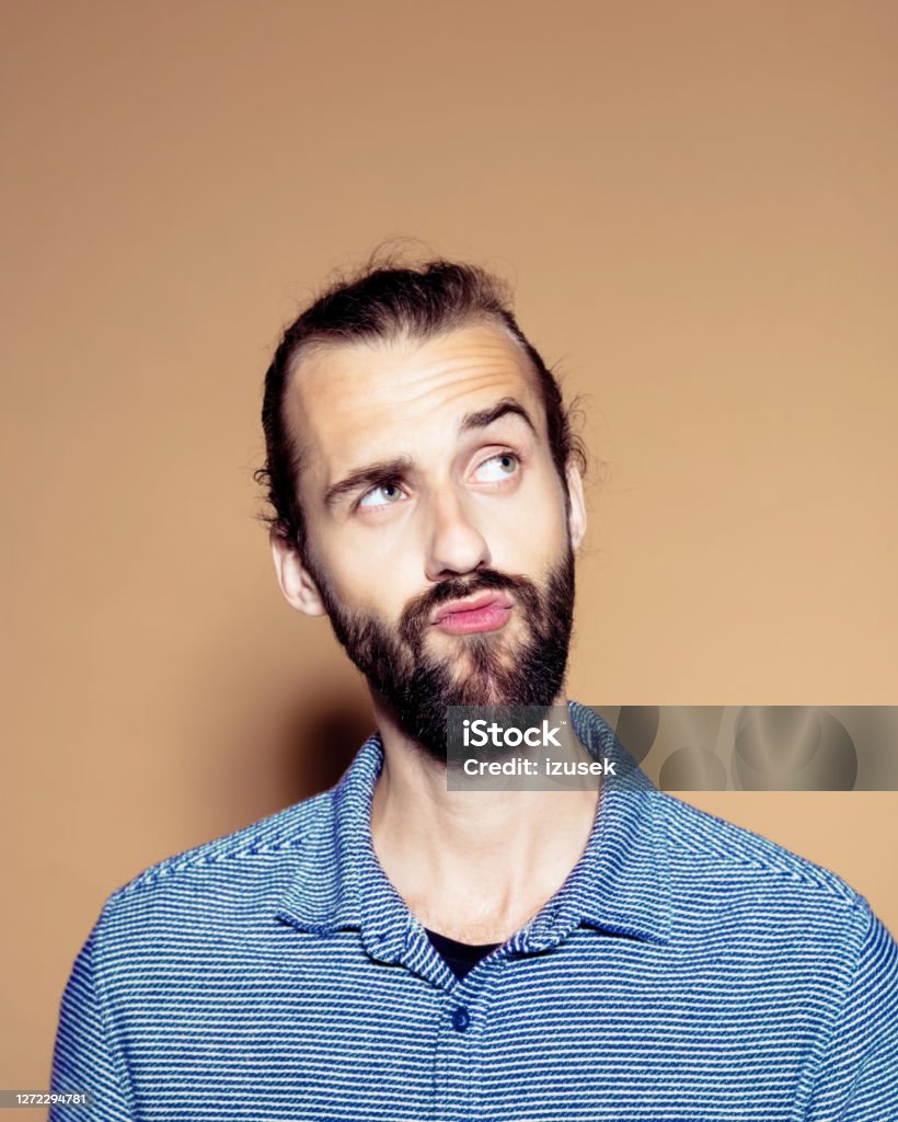 Contemplating businessman over brown background Contemplating businessman with raised eyebrow looking away. Entrepreneur standing against brown background. He is in blue shirt. 25-29 Years Stock Photo