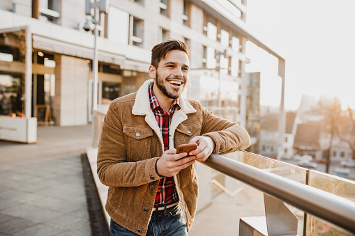 Portrait of a young man in a downtown district, smiling, holding a smartphone