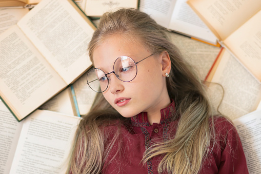Cute school girl in glasses lying on the floor. A girl is surrounded by a books.