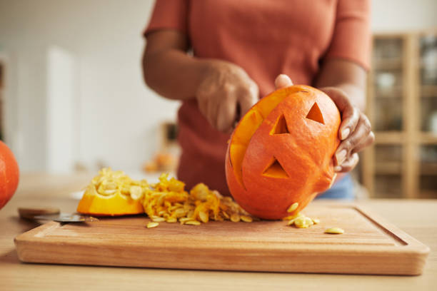 Unrecognizable Woman Carving Pumpkin Unrecognizable African American woman standing at table carving Jack-O'-Lantern out of ripe orange pumpkin carving food photos stock pictures, royalty-free photos & images