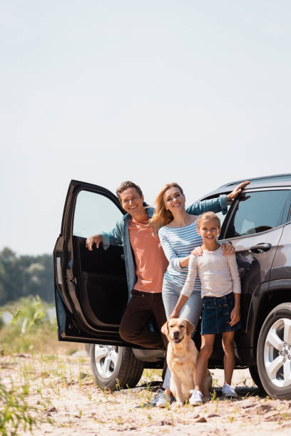 Selective focus of family with golden retriever looking at camera while standing near car outdoors Selective focus of family with golden retriever looking at camera while standing near car outdoors family in car stock pictures, royalty-free photos & images