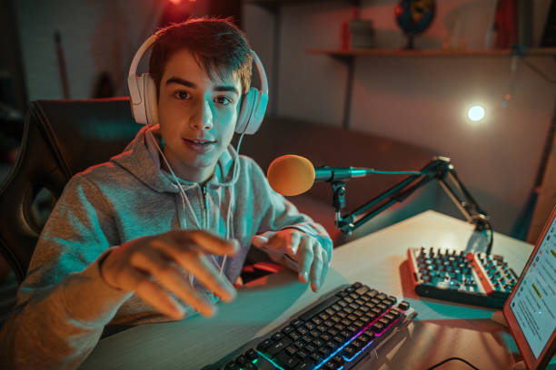 Recording vlog Teenager gamer with gaming headphones and backlight playing video game on laptop while recording, filming vlog at home. streamer photos stock pictures, royalty-free photos & images
