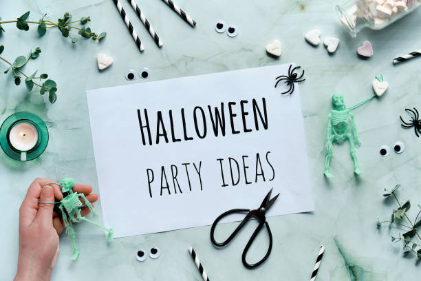 istock Clipboard with text Halloween Party ideas on mint green Halloween background. Flat lay with skeleton in hand, eucalyptus, tea light, scissors and party decorations. 1272318578