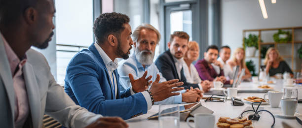 Executive Team Listening to Contrary Views from Colleague Determined African businessman expressing opinions to junior and senior colleagues on management team in conference room. organization photos stock pictures, royalty-free photos & images