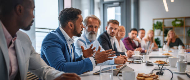 Executive Team Listening to Contrary Views from Colleague Determined African businessman expressing opinions to junior and senior colleagues on management team in conference room. group of people men mature adult serious stock pictures, royalty-free photos & images