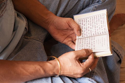 An elderly person's hand holding a brush, with their calligraphy practice placed on the table.