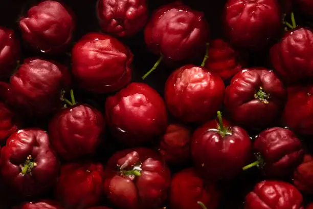 A handful of ripe acerolas, dipped in water inside dark-colored canisters.