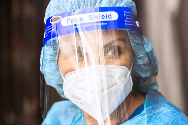 istock Tired, overworked, exhausted health care worker wearing a mask and a face shield posing looking away through a window 1272345014