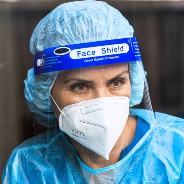 istock Tired, overworked, exhausted health care worker wearing a mask and a face shield posing looking away through a window 1272345029