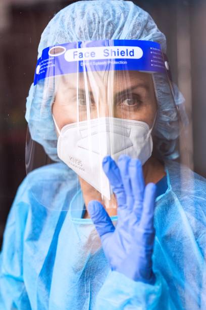 istock Tired, overworked, exhausted health care worker wearing a mask and a face shield posing looking away through a window 1272345036