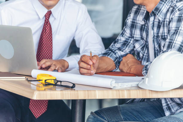 ingeniero de construcción contratista reuniéndose en la mesa de arquitectos en el sitio de construcción. hombre de negocios y gerente de ingeniero discutiendo con el proyecto de constructor de equipo de foreman utilizando cinta métrica. - hardhat construction men handshake fotografías e imágenes de stock