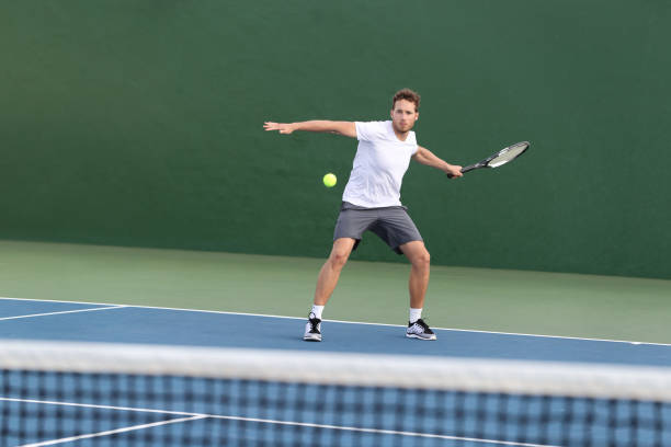 l’homme d’athlète de joueur de tennis professionnel s’est concentré sur frapper la boule au-dessus du filet sur le court dur jouant le match de tennis avec quelqu’un. sport jeu de remise en forme de vie de vie de vie de la personne vivant un mode - tennis forehand people sports and fitness photos et images de collection