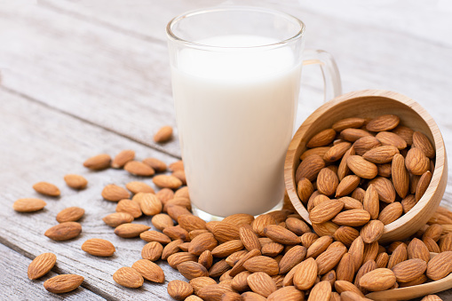 Almonds nuts in wooden bowl and almond milk in glass on wood table background.