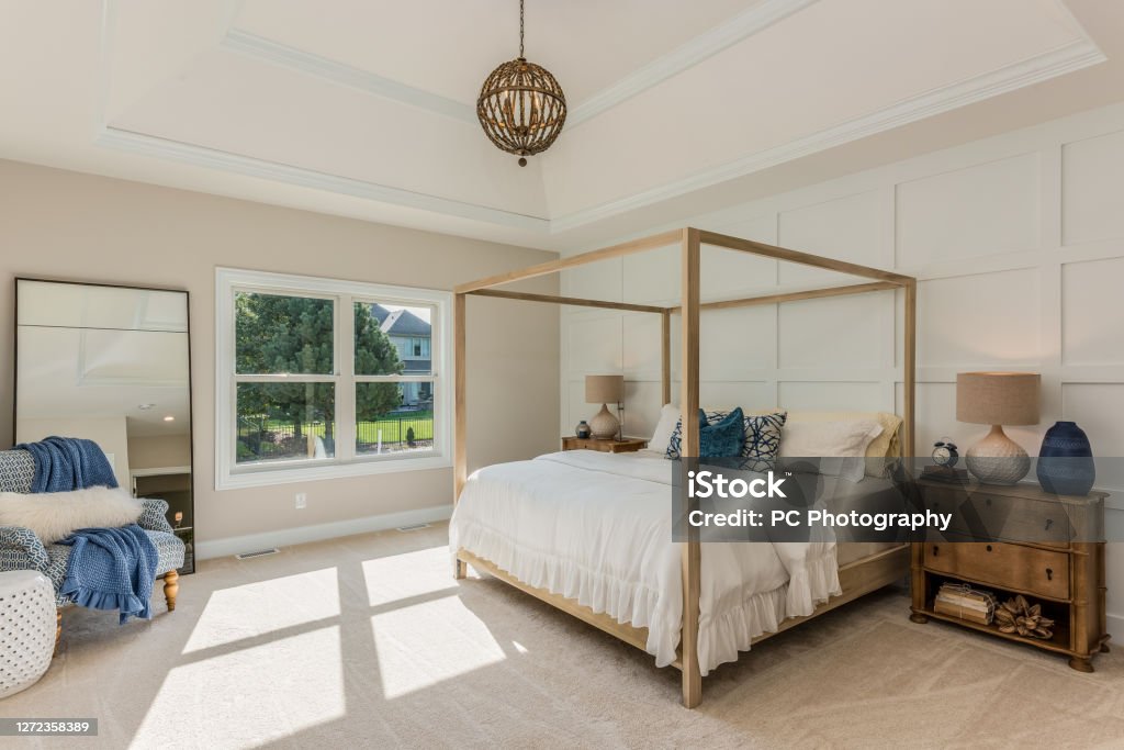 Gorgeous light and bright bedroom with four poster bed Tray ceiling with globe pendant light and decorative wall Four-Poster Bed Stock Photo