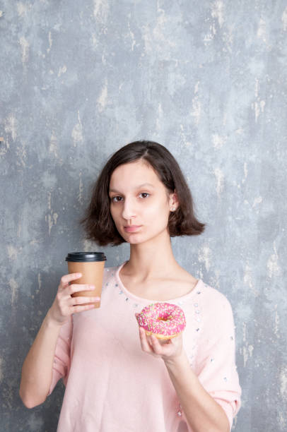 A brunette girl holds a coffee and a doughnut in her hands