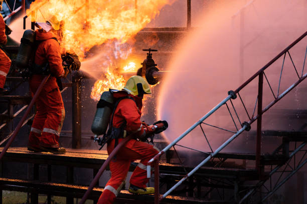 Firefighter team using water fog spraying down fire from oil rig factory explosion stock photo