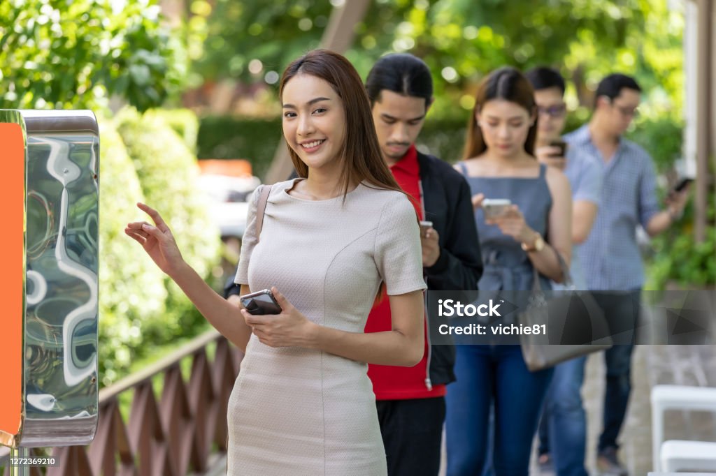Customer ordering on touch screen kiosk in restaurant. Asian woman using kiosk of food ordering with social distance queue in line before getting in fast food restaurant. Online technology self service new normal restaurant concept. Food And Drink Industry Stock Photo