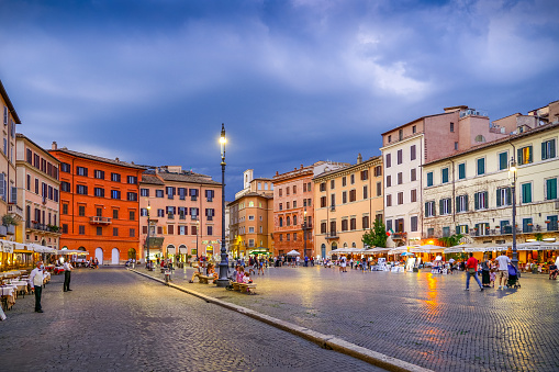 Rome, Italy, September 11 -- The first lights of the evening illuminate Piazza Navona while rain clouds gather in the sky. This iconic square in the heart of Rome is much loved by residents and tourists for the presence of many typical restaurants of Roman cuisine and for the monumental beauty of one of the most beautiful squares in the world. Image in High Definition format.