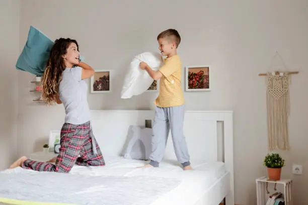Family Fun. Mother and Son Pillow Fight in Bedroom. Happy Family Games.