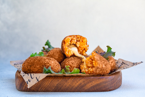 Rice balls stuffed with mozzarella cheese and deep fried on a wooden plate. Light background.